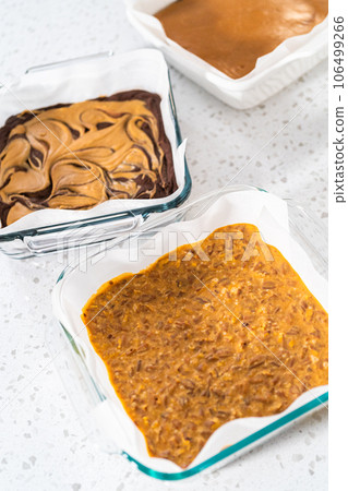 Variety of homemade fudge in square baking pans lined with parchment paper. 106499266