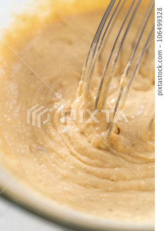 Mixing wet and dry ingredients with a hand whisk in a glass mixing bowl to prepare eggnog pancakes. 106499328