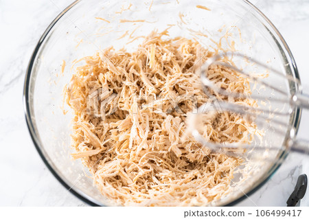 Shredded chicken in a pressure cooker. Shredding freshly cooked chicken breast in a glass mixing bowl with a hand mixer. Shredded chicken in a pressure cooker. Shredding freshly cooked chicken breast in a glass mixing bowl with a hand mixer. 106499417