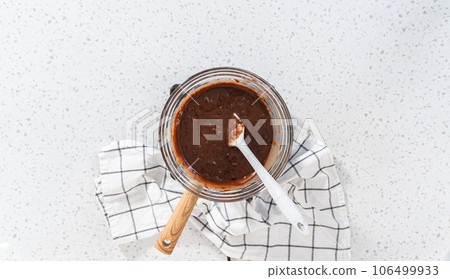 Flat lay. Melting chocolate chips and other ingredients in a glass mixing bowl over boiling water to prepare caramel fudge. Flat lay. Melting chocolate chips and other ingredients in a glass mixing bowl over boiling water to prepare caramel fudge. 106499933