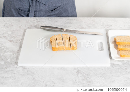 Cutting stale bread with a bread knife on a white cutting board to make croutons. Cutting stale bread with a bread knife on a white cutting board to make croutons. 106500054