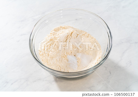 Mixing dry ingredients with a hand whisk in a glass mixing bowl to bake lemon blueberry bundt cake. Mixing dry ingredients with a hand whisk in a glass mixing bowl to bake lemon blueberry bundt cake. 106500137