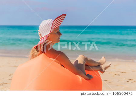 Summer lifestyle portrait of pretty girl sitting on the orange inflatable sofa on the beach of tropical island. Relaxing and enjoying life on air bed Summer lifestyle portrait of pretty girl sitting on the orange inflatable sofa on the beach of tropical island. Relaxing and enjoying life on air bed 106500475