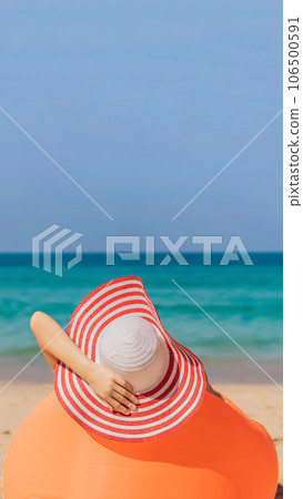Summer lifestyle portrait of pretty girl sitting on the orange inflatable sofa on the beach of tropical island. Relaxing and enjoying life on air bed VERTICAL FORMAT for Instagram mobile story or 106500591