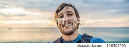 A man takes a selfie on the background of the sea and sunset BANNER, LONG FORMAT 106502063