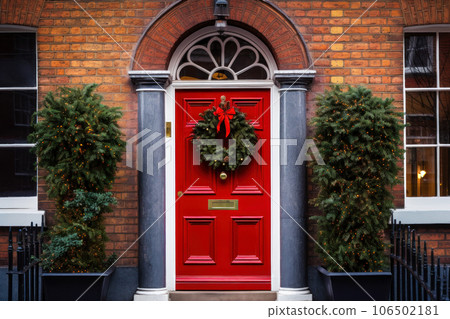 Red front door with Christmas wreath and street festive decorations on holidays Red front door with Christmas wreath and street festive decorations on holidays 106502181