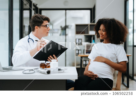 Pregnant african woman has appointment with doctor at clinic. Male gynaecologist OB GYN medic specialist with stethoscope listens to baby's heartbeat in mother's belly. Pregnancy, health care . Pregnant african woman has appointment with doctor at clinic. Male gynaecologist OB GYN medic specialist with stethoscope listens to baby's heartbeat in mother's belly. Pregnancy, health care . 106502258