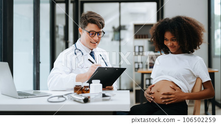 Pregnant african woman has appointment with doctor at clinic. Male gynaecologist OB GYN medic specialist with stethoscope listens to baby's heartbeat in mother's belly. Pregnancy, health care . Pregnant african woman has appointment with doctor at clinic. Male gynaecologist OB GYN medic specialist with stethoscope listens to baby's heartbeat in mother's belly. Pregnancy, health care . 106502259