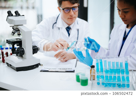 Focused mature male doctor and African female nurse look at tablet and laptop screen discuss anamnesis together. Concentrated diverse medical professionals 106502472