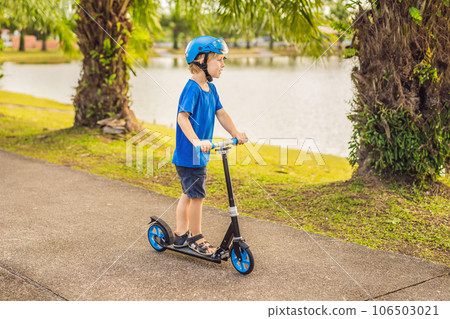 Boy riding scooters, outdoor in the park, summertime. Kids are happy playing outdoors Boy riding scooters, outdoor in the park, summertime. Kids are happy playing outdoors 106503021