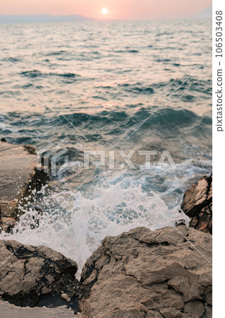 A sea wave hits a stone and rock on the coast. Sea sunset 106503408