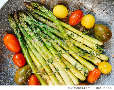 Green asparagus with whole tomatoes and herbs fried in oil in a pan Green asparagus with whole tomatoes and herbs fried in oil in a pan 106504854