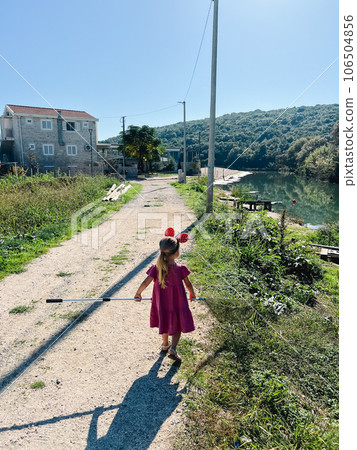Little girl with Minnie Mouse ears on her head and a landing net in her hands walks along the river bank Little girl with Minnie Mouse ears on her head and a landing net in her hands walks along the river bank 106504856