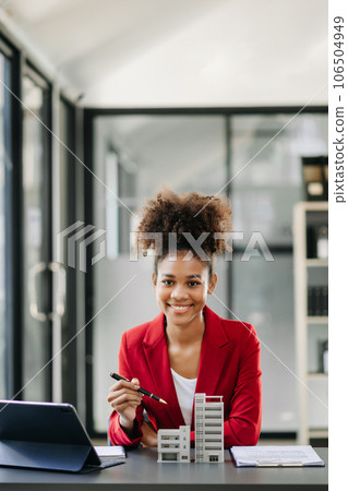 Young real estate agent worker working with laptop and tablet at table in office and small house beside it. Young real estate agent worker working with laptop and tablet at table in office and small house beside it. 106504949