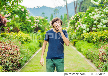 Young man blowing nose in front of blooming tree. Spring allergy concept 106505094