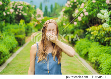 Young pretty woman blowing nose in front of blooming tree. Spring allergy concept 106505119