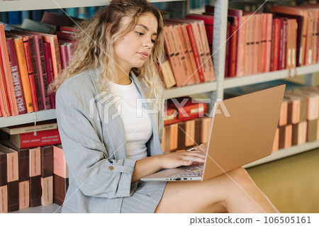 Beautiful female freshman using laptop in public library. Woman sitting on floor  106505161