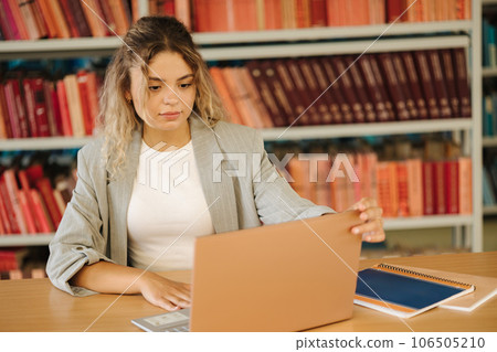 Young female student open laptop and start studying in public library. Woman preparing for university examination Young female student open laptop and start studying in public library. Woman preparing for university examination 106505210