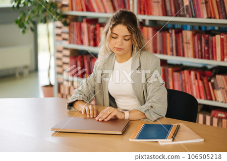 Young female student open laptop and start studying in public library. Woman preparing for university examination Young female student open laptop and start studying in public library. Woman preparing for university examination 106505218