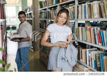 Handsome boy looking on beautiful girl in library. Two person in university library. Acquaintance in the library Handsome boy looking on beautiful girl in library. Two person in university library. Acquaintance in the library 106505246