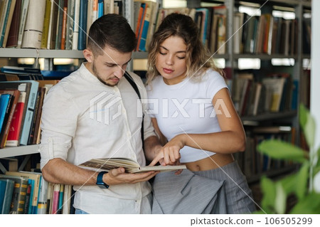 Handsome man and attractive female looking for book in university library. Woman show something to classmate in book Handsome man and attractive female looking for book in university library. Woman show something to classmate in book 106505299