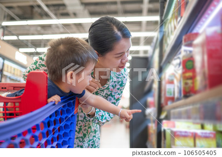 Asian mom and her little multiracial boy in shopping trolley are shopping for groceries in the supermarket Asian mom and her little multiracial boy in shopping trolley are shopping for groceries in the supermarket 106505405