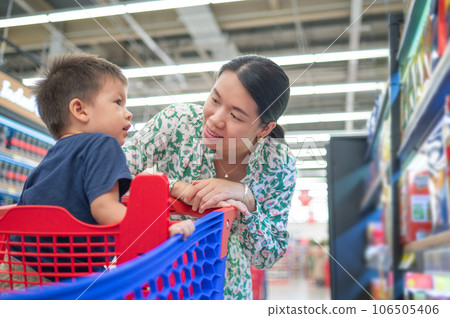 Asian mom and her little multiracial boy in shopping trolley are shopping for groceries in the supermarket Asian mom and her little multiracial boy in shopping trolley are shopping for groceries in the supermarket 106505406