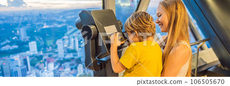 Mom and son are looking at Kuala lumpur cityscape. Use binoculars. Panoramic view of Kuala Lumpur city skyline evening at sunset skyscrapers building in Malaysia. Traveling with kids concept BANNER Mom and son are looking at Kuala lumpur cityscape. Use binoculars. Panoramic view of Kuala Lumpur city skyline evening at sunset skyscrapers building in Malaysia. Traveling with kids concept BANNER 106505670