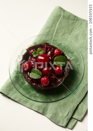 chocolate dessert with lingonberry jam, cherries and mint on a transparent plate 106505935