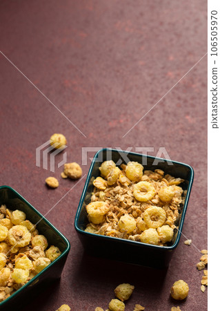 Breakfast cereal with granola and corn rings in bowls on maroon background 106505970