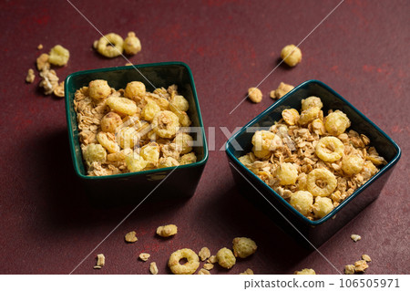 Breakfast cereal with granola in small bowls on maroon background 106505971