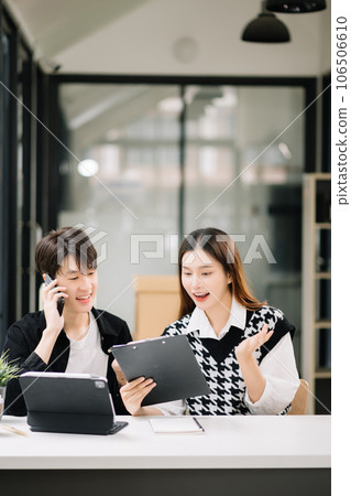 Two Asian business workers talking on the smartphone and using laptop at the modern office. Two Asian business workers talking on the smartphone and using laptop at the modern office. 106506610
