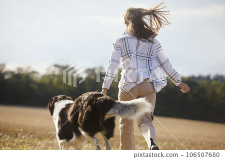 Happy teen girl with her dog runing across field. 106507680
