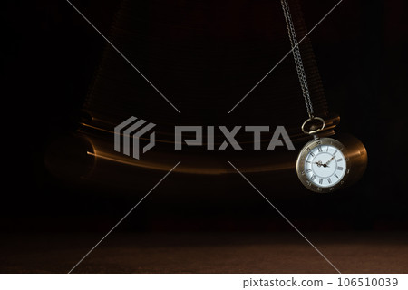 Hypnosis session. Vintage pocket watch with chain swinging over surface on dark background among faded clock faces, magic motion effect 106510039