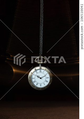 Hypnosis session. Vintage pocket watch with chain swinging over surface on dark background among faded clock faces, magic motion effect 106510041