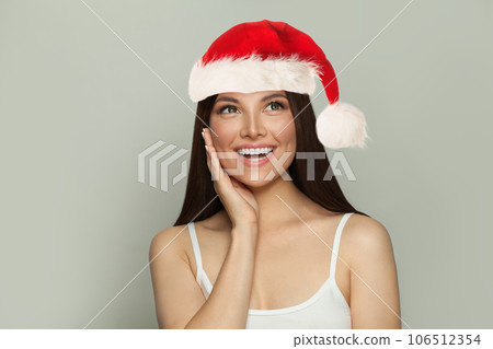 Happy smiling Christmas woman in Santa hat looking up on grey background Happy smiling Christmas woman in Santa hat looking up on grey background 106512354