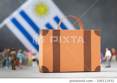 Cardboard suitcase, plastic toy people and a flag on an abstract background, a concept on the theme of moving or migration in Uruguay Cardboard suitcase, plastic toy people and a flag on an abstract background, a concept on the theme of moving or migration in Uruguay 106512432