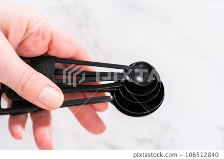 Close-up view. Black metal measuring spoons for baking on a marble countertop. 106512840