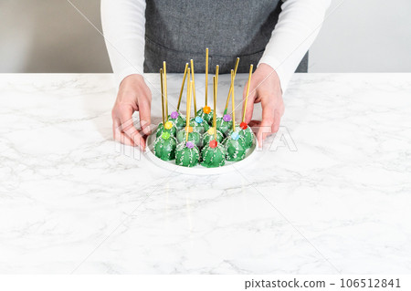 Cactus-shaped cake pops, beautifully decorated with luster dust, sugar flowers, and white sprinkles, arranged in celebration of Cinco de Mayo. 106512841