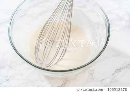Mixing ingredients in a large glass mixing bowl to make homemade royal icing. 106512878
