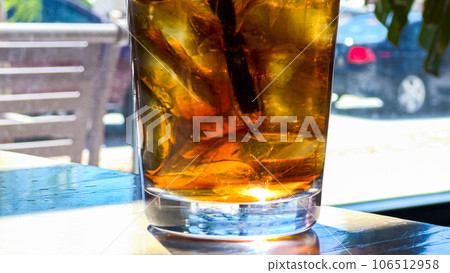 A close-up shot showcases a refreshing glass filled with ice cubes and soda pop, placed on a restaurant table, inviting the viewer to enjoy a cool and fizzy beverage. A close-up shot showcases a refreshing glass filled with ice cubes and soda pop, placed on a restaurant table, inviting the viewer to enjoy a cool and fizzy beverage. 106512958