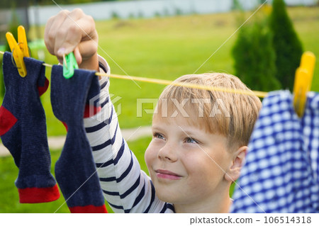 A happy caucasian 9 years boy helps her mother to hang up clothes. Development of fine motor skills through household activities. Selective focus. A happy caucasian 9 years boy helps her mother to hang up clothes. Development of fine motor skills through household activities. Selective focus. 106514318