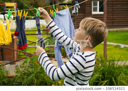 A happy caucasian 9 years boy helps her mother to hang up clothes. Development of fine motor skills through household activities. Selective focus. 106514321