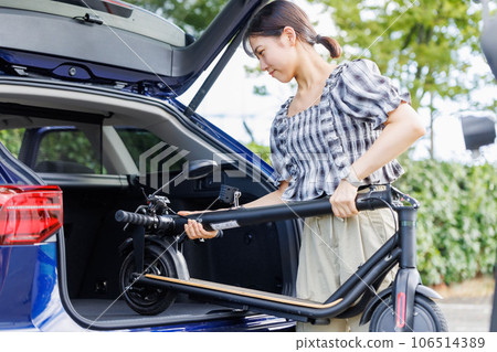 A woman putting an electric scooter on a car 106514389