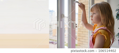 Banner safety at home for small children. a lock on the window protects children from opening the window. The girl 4 years old tries to open the window standing on the windowsill on a high floor. Banner safety at home for small children. a lock on the window protects children from opening the window. The girl 4 years old tries to open the window standing on the windowsill on a high floor. 106514402