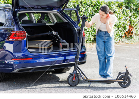 A woman trying to load an electric kickboard into a car A woman trying to load an electric kickboard into a car 106514460