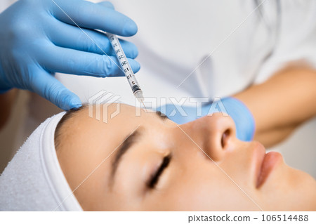 Young woman getting a rejuvenating facial injection in the clinic. Professional application of botox and hyaluronic acid. Young woman getting a rejuvenating facial injection in the clinic. Professional application of botox and hyaluronic acid. 106514488
