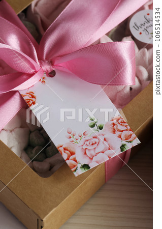 Homemade marshmallows in a paper gift box. Zephyr flowers. The box is tied with a ribbon tied into a bow. Tag with a field for the text. Close-up. Homemade marshmallows in a paper gift box. Zephyr flowers. The box is tied with a ribbon tied into a bow. Tag with a field for the text. Close-up. 106514534