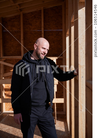 Male architect building wooden frame house. Bald man standing on construction site, inspecting quality of work on sunny day. Male architect building wooden frame house. Bald man standing on construction site, inspecting quality of work on sunny day. 106514546