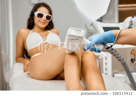 Laser epilation procedure for happy young woman in protective goggles and bikini in clinic center. Laser epilation procedure for happy young woman in protective goggles and bikini in clinic center. 106515412